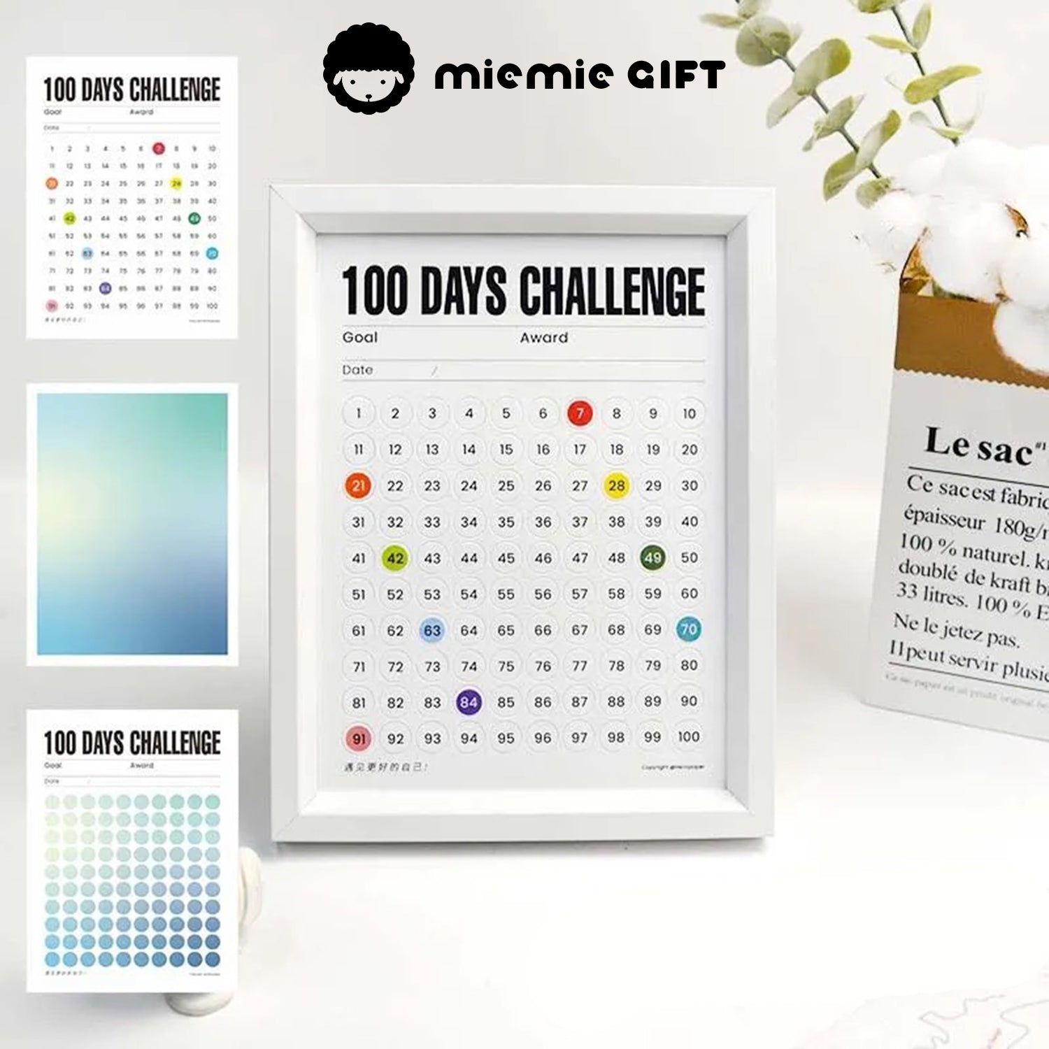 A white-framed 100 Days Challenge tracker is displayed alongside additional gradient paper options, including vibrant blue and green tones. The frame is paired with a minimalist cotton branch vase, emphasizing its functional and decorative appeal for any space.