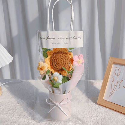 Miniature hand-knit flower arrangement with a vibrant sunflower centerpiece and dainty accents in gift bag with clear window
