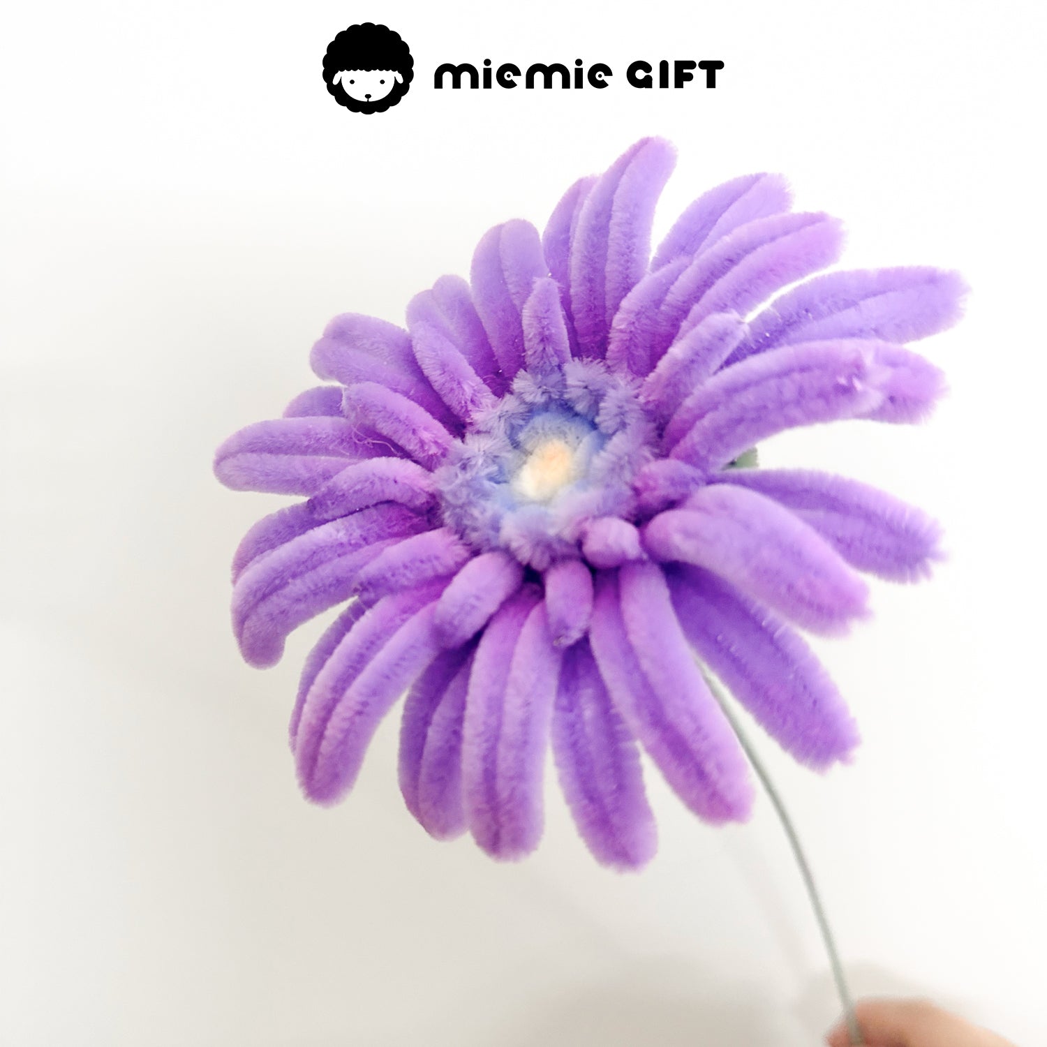 Close-up view of a handmade purple frangipani flower made with pipe cleaners, showcasing delicate craftsmanship.