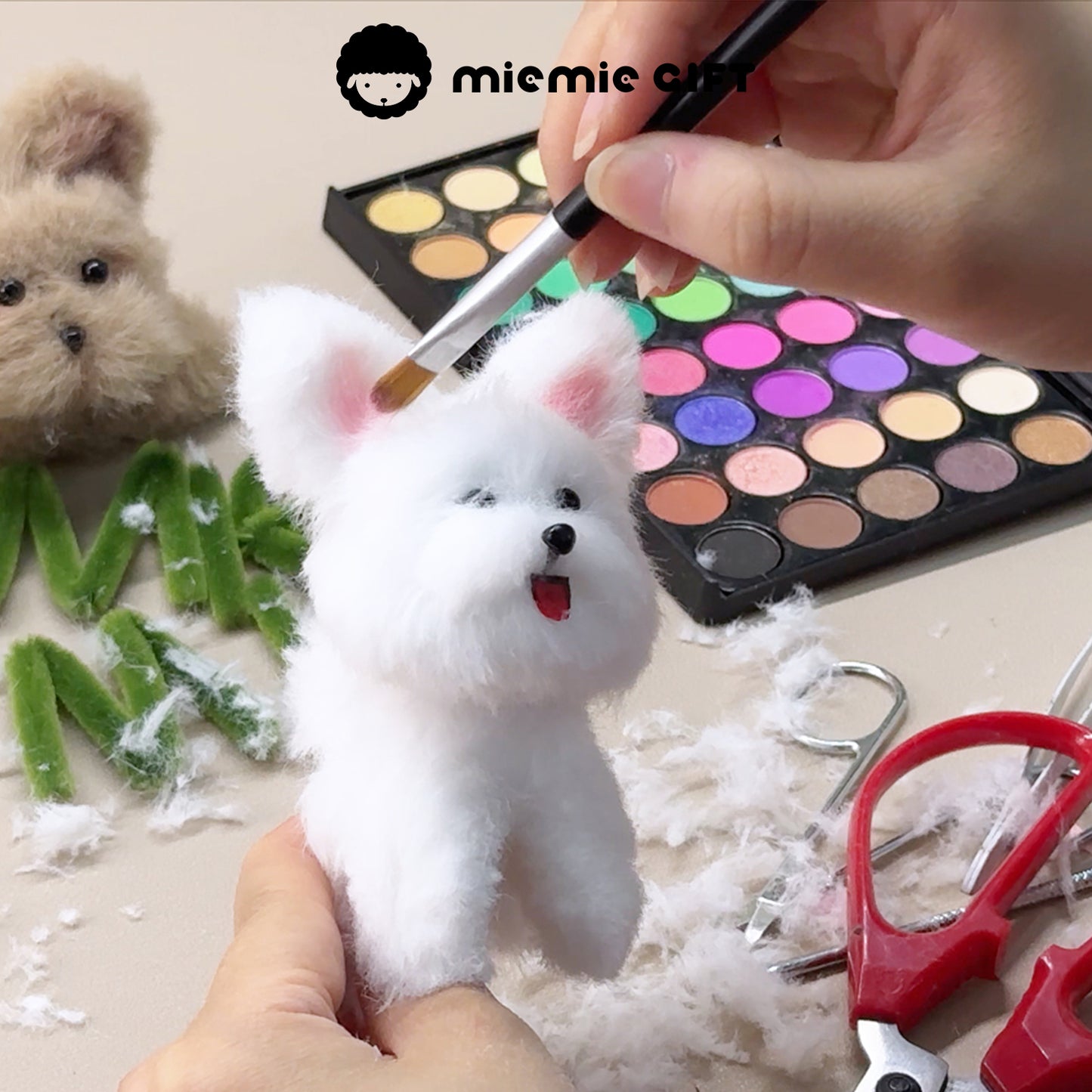 A hand is using the MieMie Gift 40-Color DIY Chalk Powder Palette to add color to a fluffy white pipe cleaner dog craft. The background features green pipe cleaners, scissors, and a brown pipe cleaner dog, showcasing the creative application of the chalk powder for DIY projects.