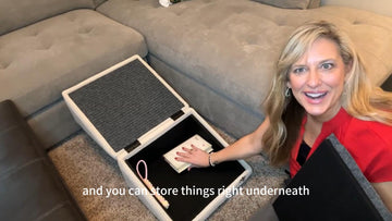 Woman demonstrating the hidden storage compartment inside a foldable dog ramp beside a sectional sofa.