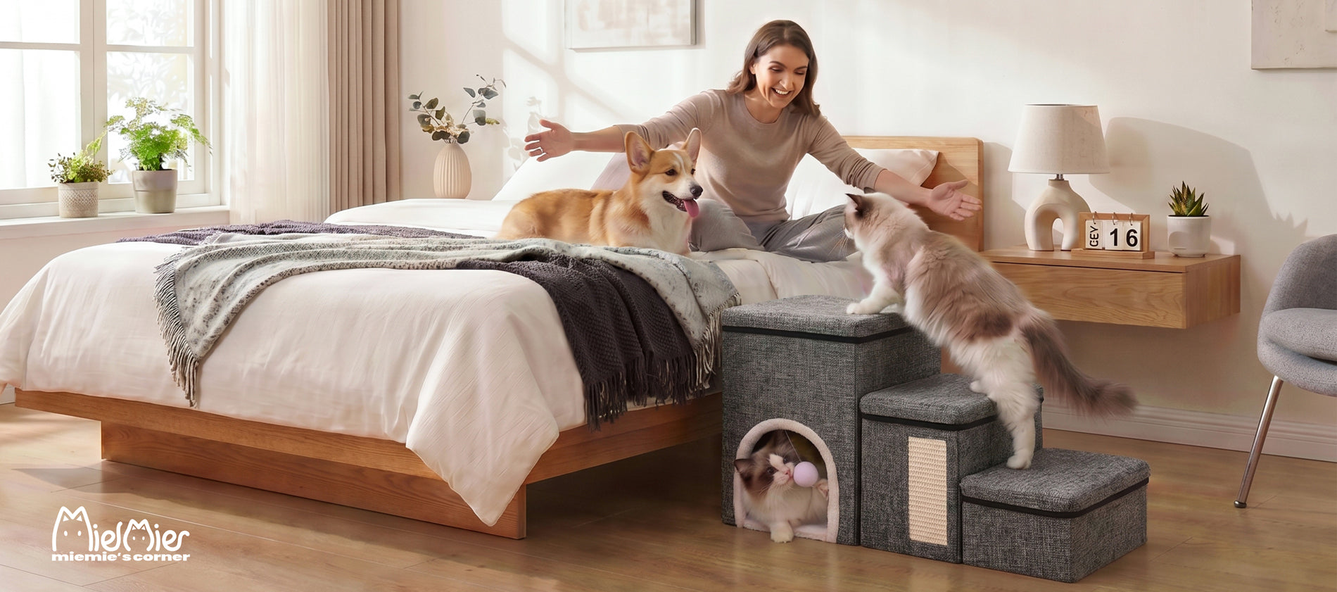 A cat climbing foldable pet stairs beside a bed while another cat rests in the hideaway and a dog sits with its owner on the bed.