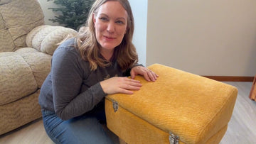 Woman kneeling beside a mustard yellow dog ramp folded into an ottoman in a living room.